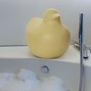 Scultura decorativa home decor in shape of a yellow duck placed next to a bathtub with bubbles.